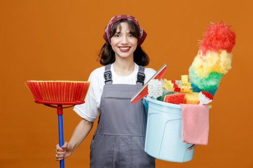 smiling-young-female-cleaner-wearing-uniform-bandana-holding-squeegee-mop-bucket-cleaning-tools-looking-camera-isolated-orange-background-1.jpg